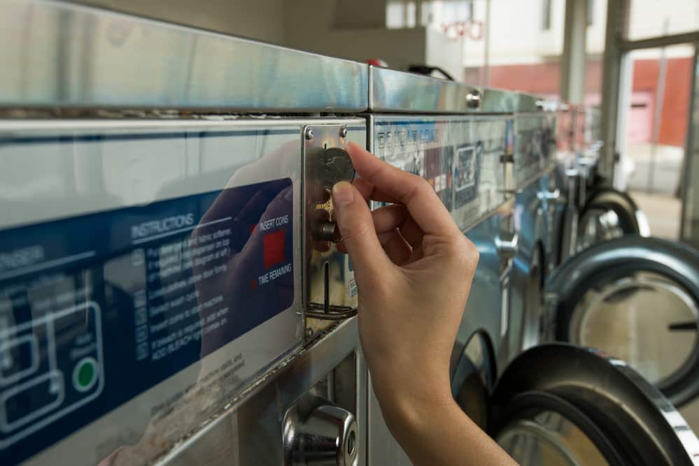 Close-up of hand inserting quarter into laundry machine in laundromat