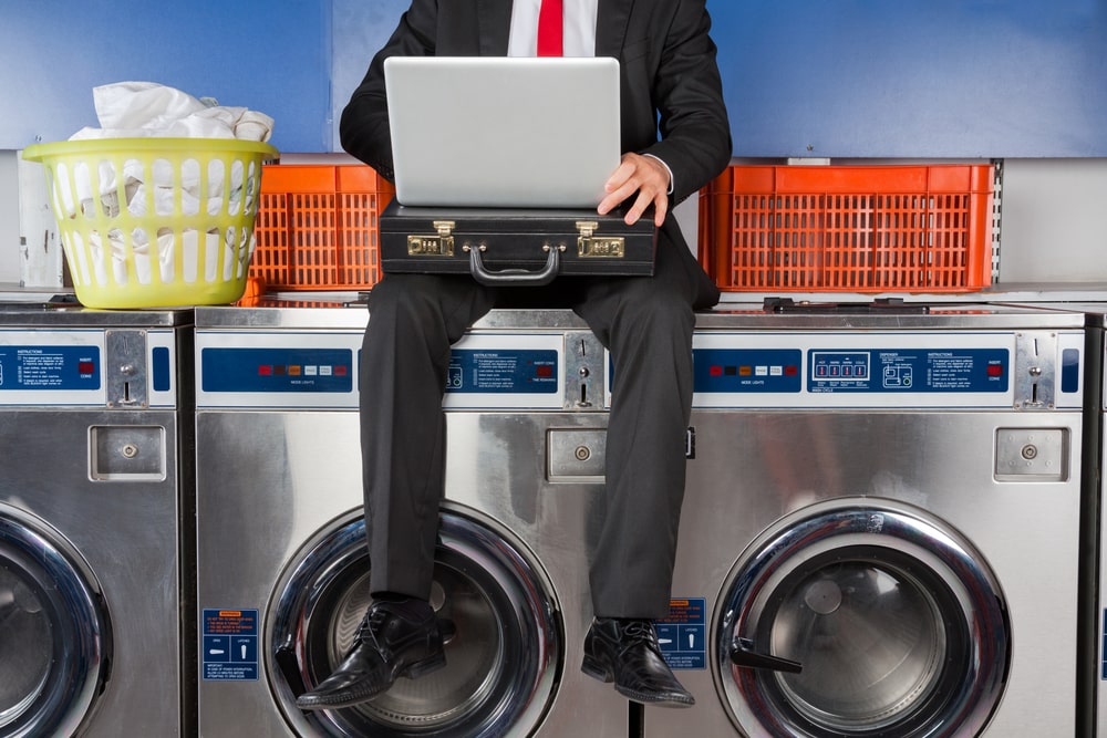 Businessman in suit looking at laptop while sitting on washer at laundromat