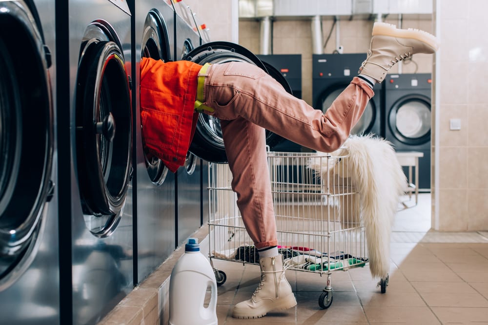 Woman sticking her head and shoulders into washing machine at laundromat, kicking up foot