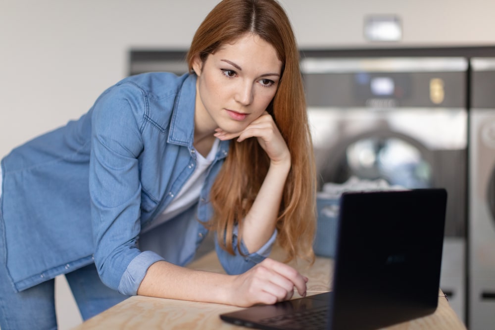 Young woman using laptop at the laundromat