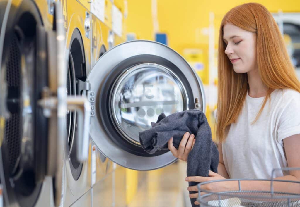 Young woman using washer at laundromat